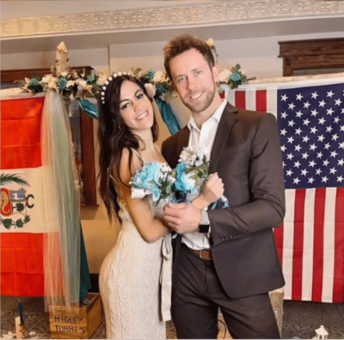 unos novios en una imagen el día de su boda atrás de ellos colocaron las banderas de sus países