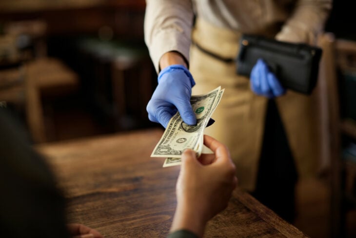 mano de una persona dándole unos billetes de propina a un mesero en un restaurante 