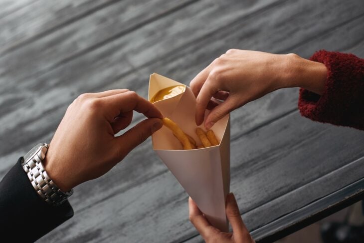 manos de una pareja comiendo papas fritas de un cono de papel 