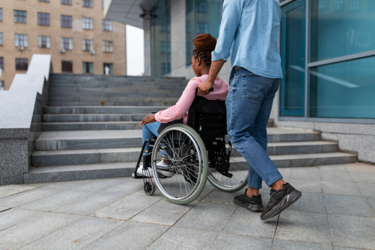 Fotografía que muestra a un hombre empujando a su novia en silla de ruedas por la calle 