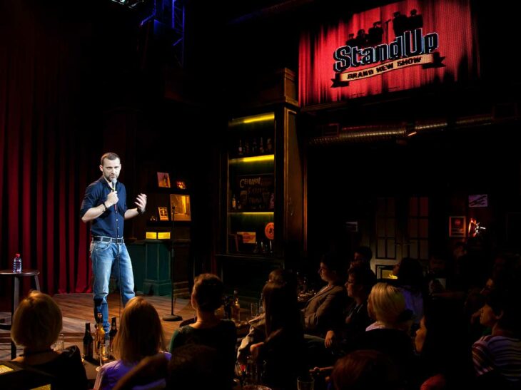 Hombre parado en el escenario de un bar frente a la gente presentando su show de stand up 