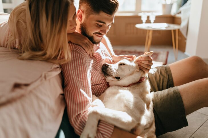 pareja sentada en una recámara mientras ven dormir a su perro 