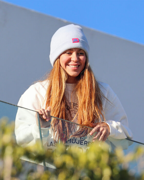 Photograph of Shakira leaning out on the balcony of her house wearing a sweatshirt and a hat on her head