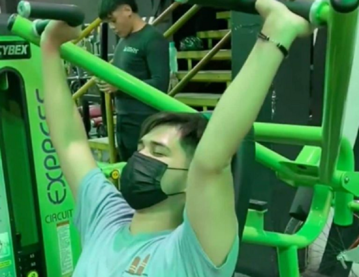 un joven en un aparato de gimnasio que trabaja los músculos de los brazos