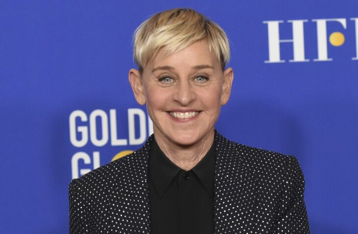 Ellen DeGeneres smiling on a red carpet wears dark clothing