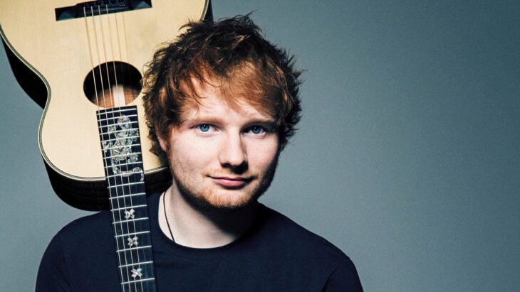 Ed Sheeran sostiene una guitarra al revés con su hombro lleva ropa oscura