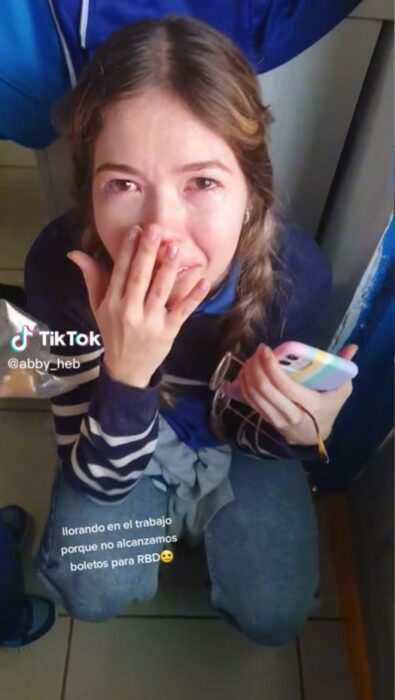 captura de pantalla de una mujer llorando con la mano en su cara y un celular en la otra 