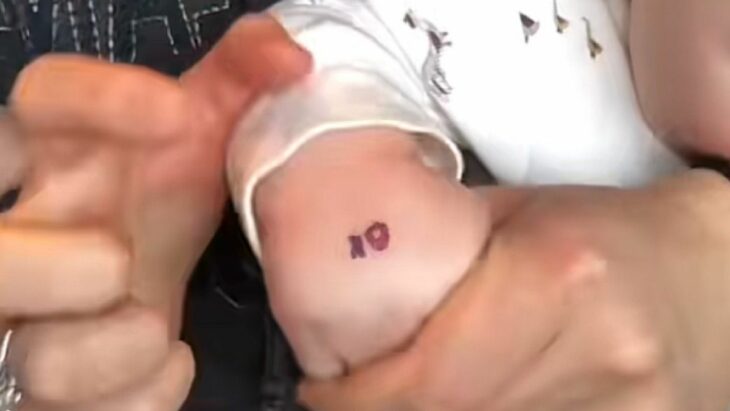 image of a woman showing her baby's hand with a water tattoo with the letters KO