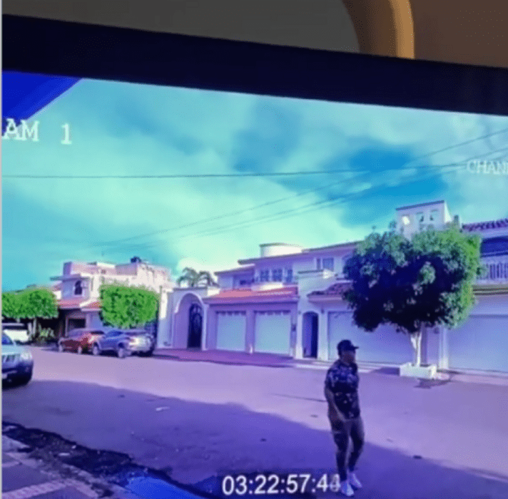 un hombre camina por una calle viste ropa estilo militar en un vecindario de casas grandes