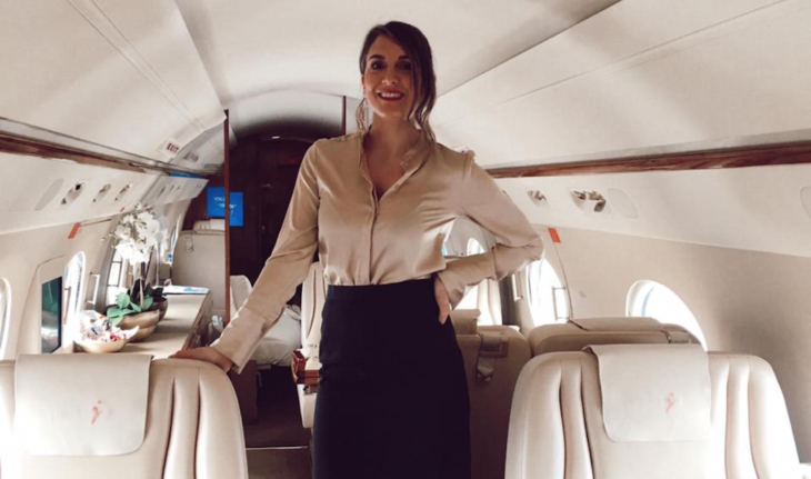 una sobrecargo de aviación vestida con elegancia está de pie en el interior de un jet privado
