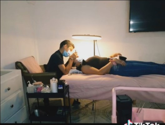 Fotografía de un chico de 13 años aplicando extensiones de pestañas a una mujer acostada sobre una cama 