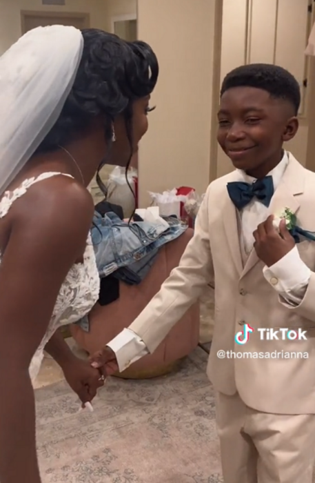 un chico sonríe feliz mientras toma de la mano a su madre quien está vestida de novia