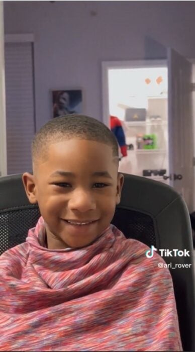 image showing a boy sitting smiling after his father cuts his hair 