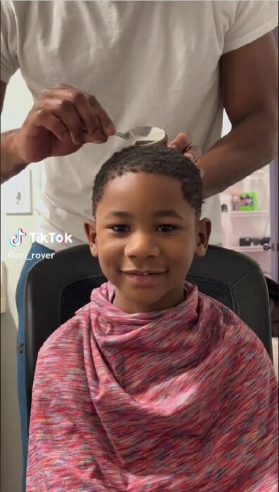 photograph of a boy sitting while his father cuts his hair with a spoon 