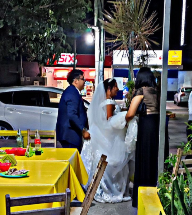some bride and groom walk down the street next to a taco shop wearing their wedding suits 