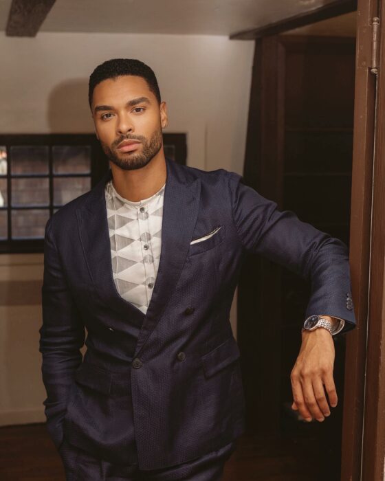 photograph of British actor Reg+e-Jean Page posing in a suit with one arm leaning against a wall