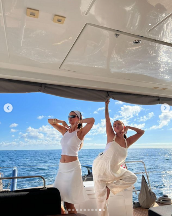 Selena Gomez y Nicola Peltz bailan en una yate en alta mar llevan outfits de playa en color blanco es de día