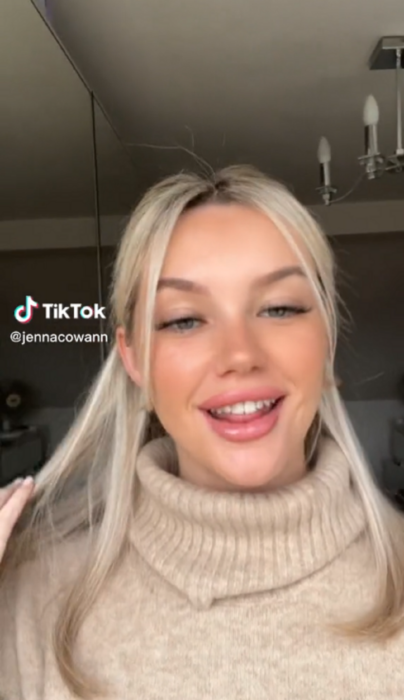 una chica caucásica lleva el cabello en media coleta lacio y largo está sonriendo a la cámara porta un suéter color crema imagen de TikTok