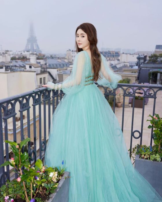 Abby Choi posando con la mano sobre un barandal con la Torre Eiffel de fondo