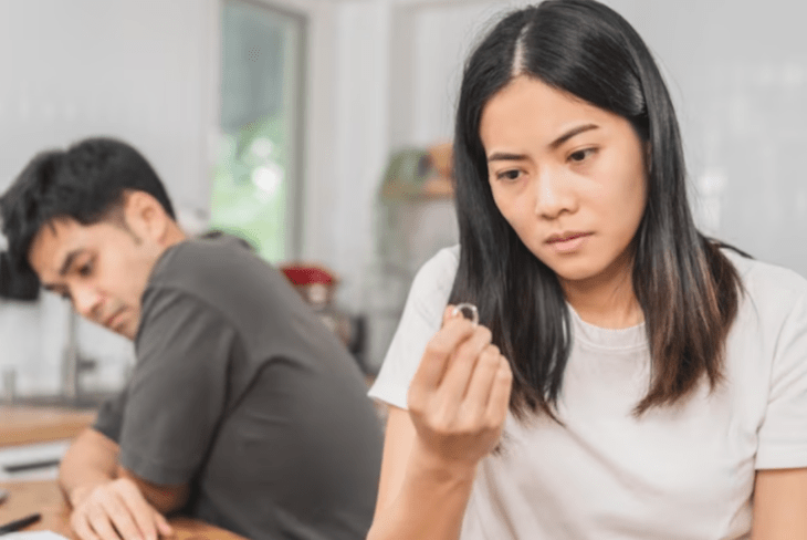 una pareja de esposos chinos peleando ella sostiene su anillo de casada con su mano él está reflexivo