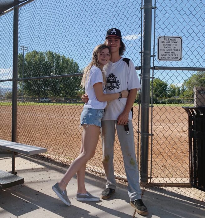 fotografía de una chica abrazando a un chico frente a lo que parece ser una cancha de beisbol 