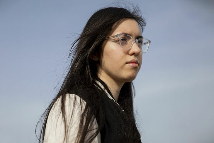 una chica con anteojos viendo al horizonte lleva una chamarra universitaria