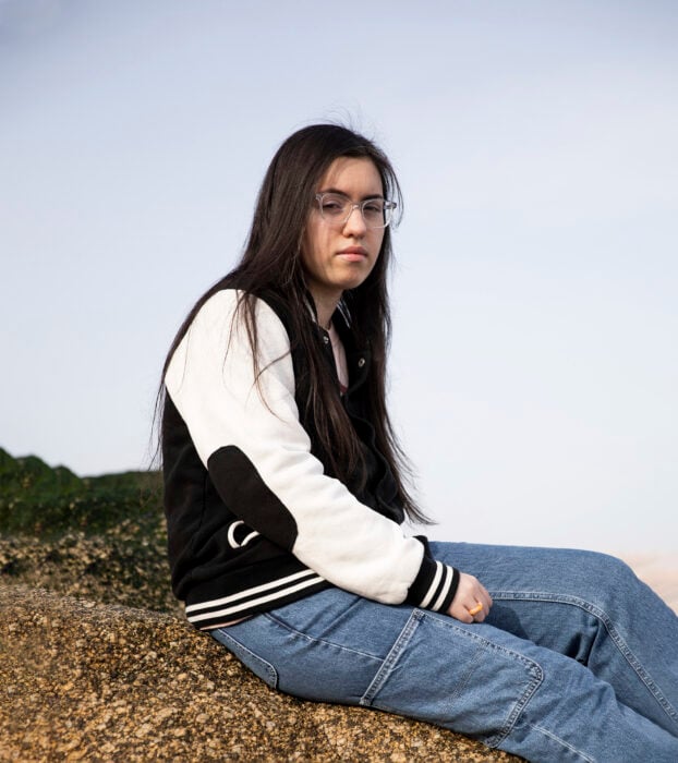 un chica sentada sobre una roca con una mirada triste lleva jeans y chamarra universitaria 