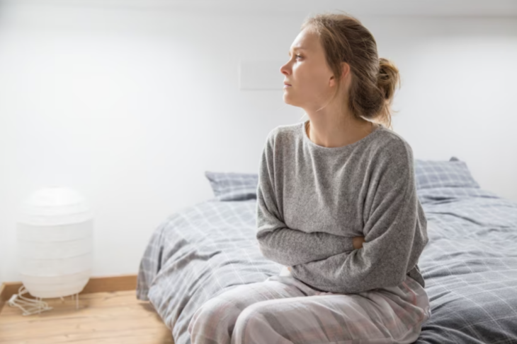 una mujer se toca el vientre por cólicos menstruales está sentada en una cama y trae puesta una pijama