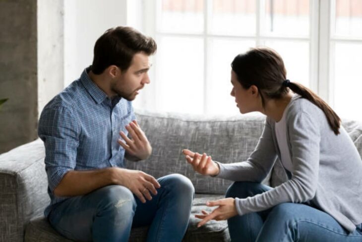 una aparente pareja discute mientras están sentados en un sillón gris 