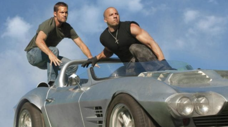Vin Diesel y Paul Walker en una escena de la película Rápidos y furiosos están sobre un auto gris