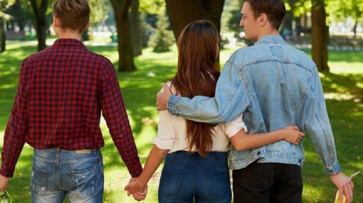 imagen de una chica con dos hombres de espaldas caminando abrazada con uno y tomada de la mano con el otro