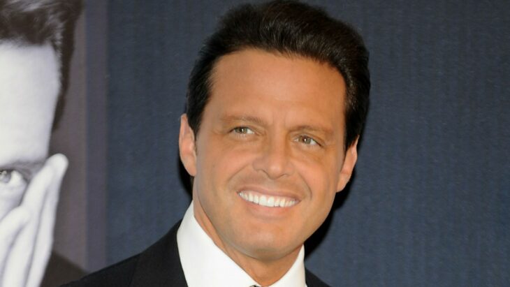 imagen de Luis Miguel está sonriendo y lleva un traje oscuro con corbata y una camisa blanca