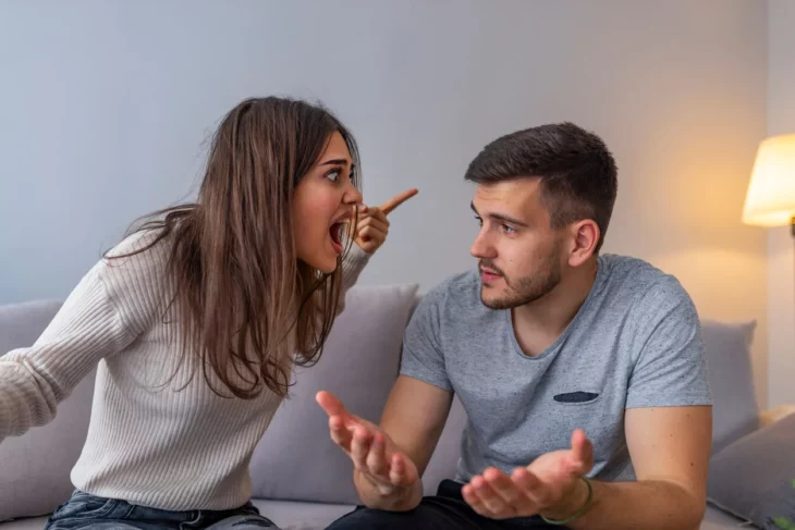 a woman yelling angrily at a man are sitting in an armchair