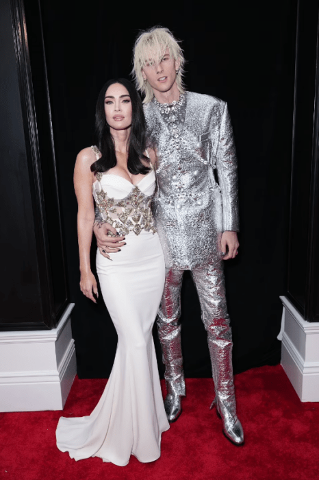 Megan Fox y Machine Gun Kelly en una imagen de cuerpo entero ambos están vestidos en colores claros y parados sobre una alfombra roja