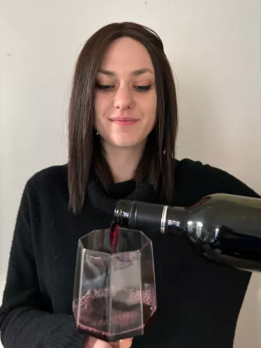 una chica sirviendo una copa con una botella de vino tinto