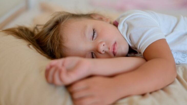 una niña de cinco años dormida en su cama lleva una playerita blanca