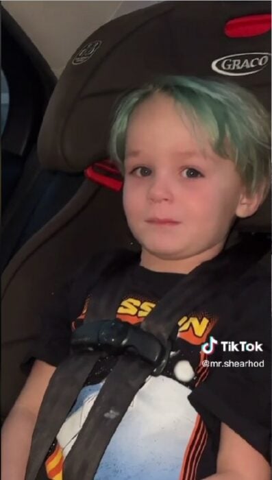 captura de pantalla que muestra a un niño con el cabello verde sentado en el asiento de un carro 