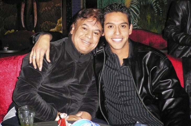 Juan Gabriel y su hijo Iván Aguilera están sentados y abrazados cariñosamente ambos visten de color negro