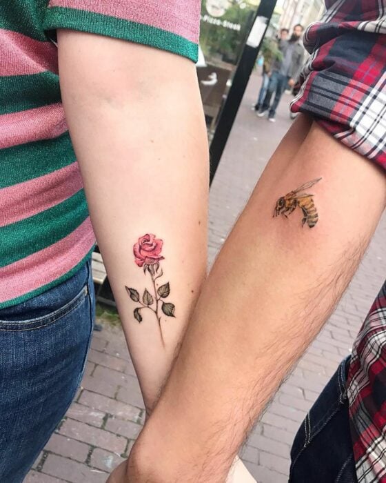 brazos de una pareja mostrando sus tatuajes de una rosa y una abeja 
