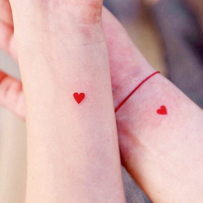 brazos de unas personas mostrando un pequeño tatuaje en color rojo 