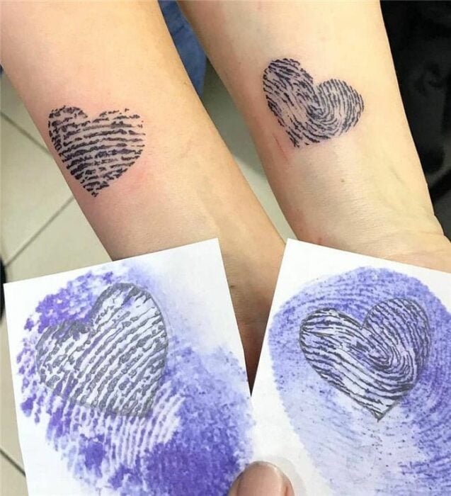 dos brazos con mostrando un tatuaje de corazón formado con las huellas de dos personas 