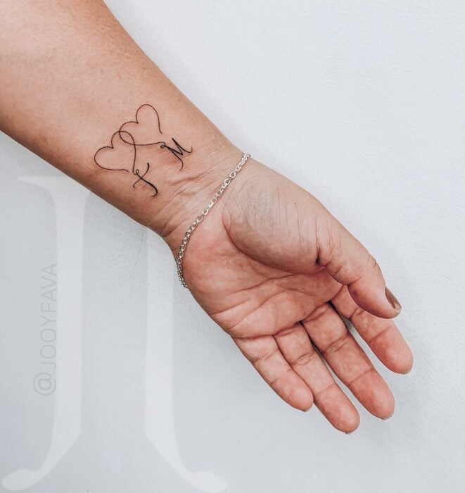 mano de una mujer mostrando un tatuaje de las letras F y M bajo un corazón 