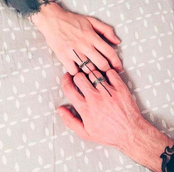 manos de dos personas unidas para complementar un tatuaje de parejas en el dedo anular