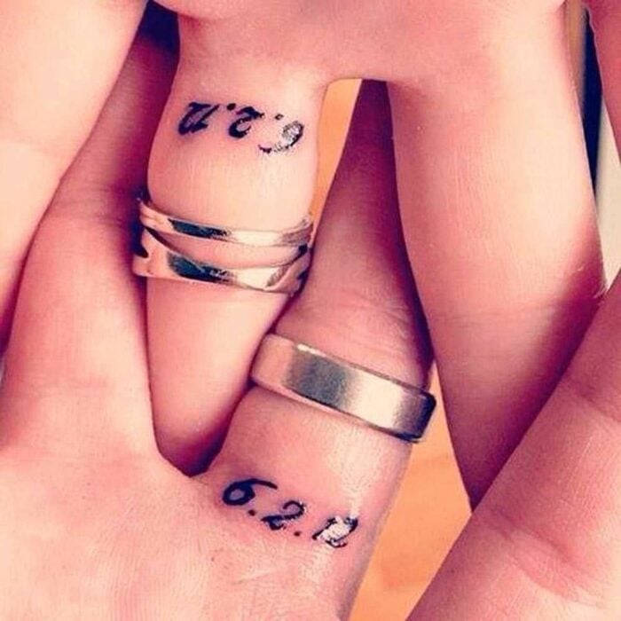 dedos de dos personas juntas en las que muestran un tatuaje de fecha 