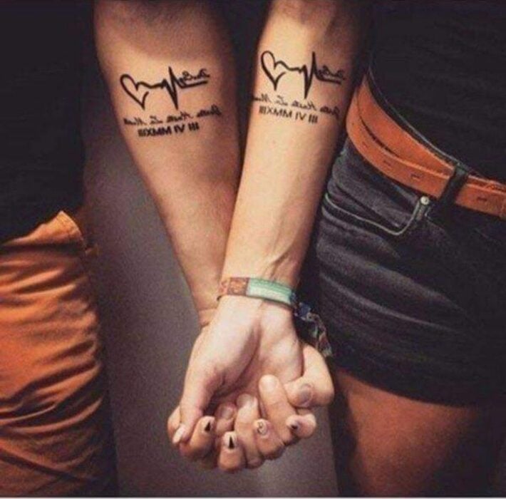 pareja mostrando su diseño de tatuaje con un corazón y electro sobre una frase 