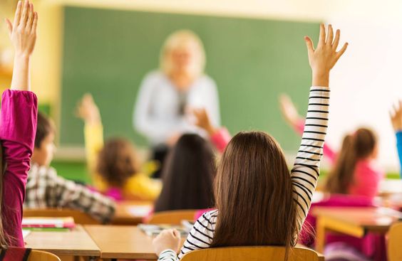 niños de espaldas levantando la mano en clase