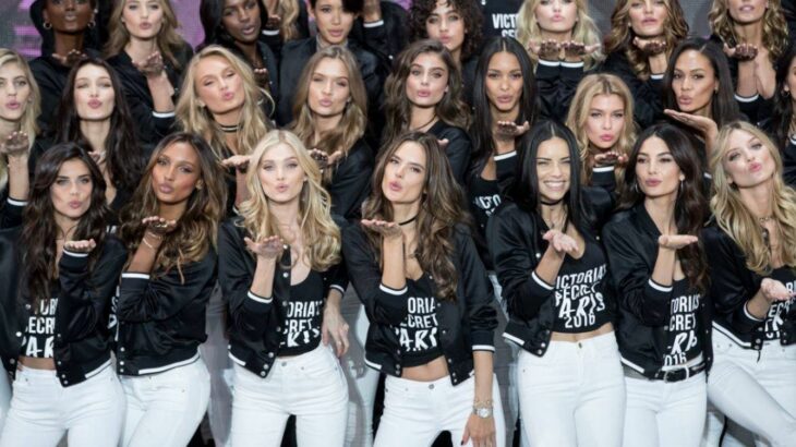 Victoria's Secret models blow a kiss to the camera all wear identical clothes black jacket and white pants 