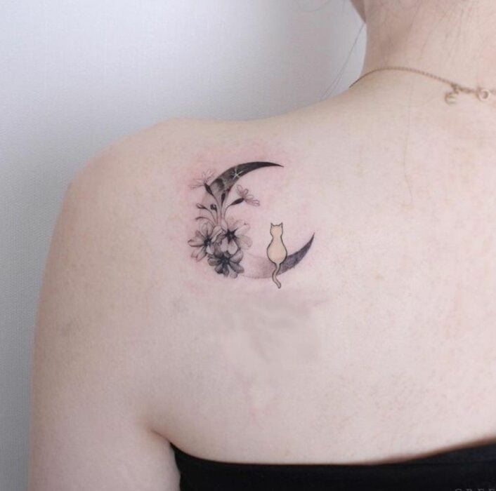 espalda de una chica mostrando el tatuaje de una luna con flores y un gato 