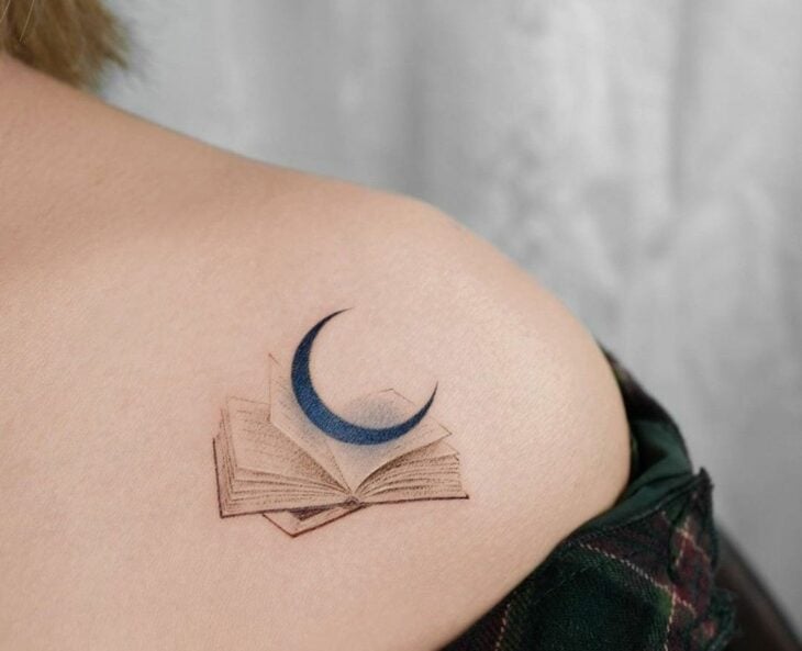 tatuaje de una luna con un libro en la clavícula de una mujer 