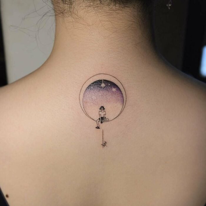 espalda de una chica mostrando el diseño de tatuaje de una luna con una chica sentada dentro de ella 